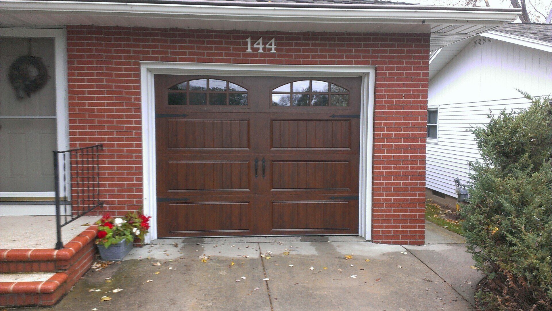 Brick house garage with wooden double doors, house number 144, and a flower planter by the steps
