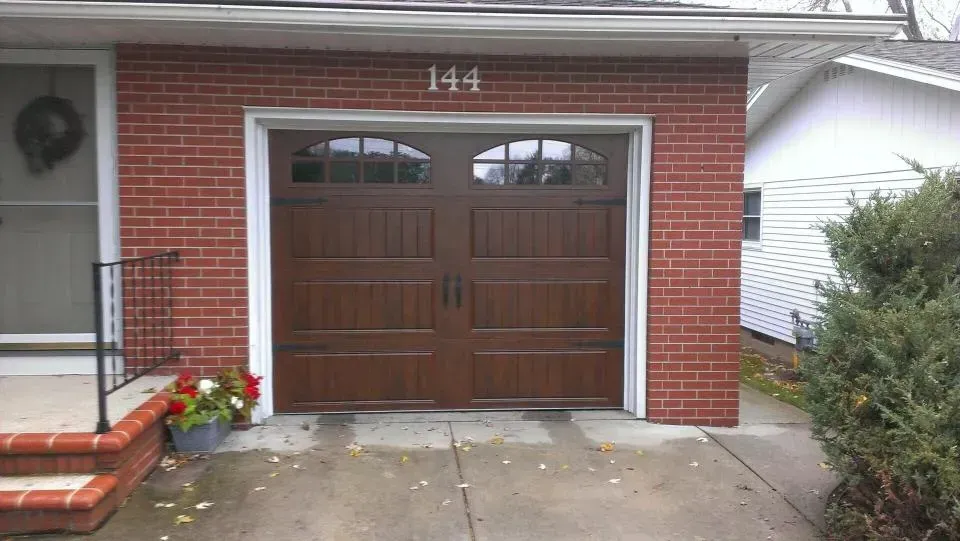 Brick house garage with wooden double doors, house number 144, and a flower planter by the steps