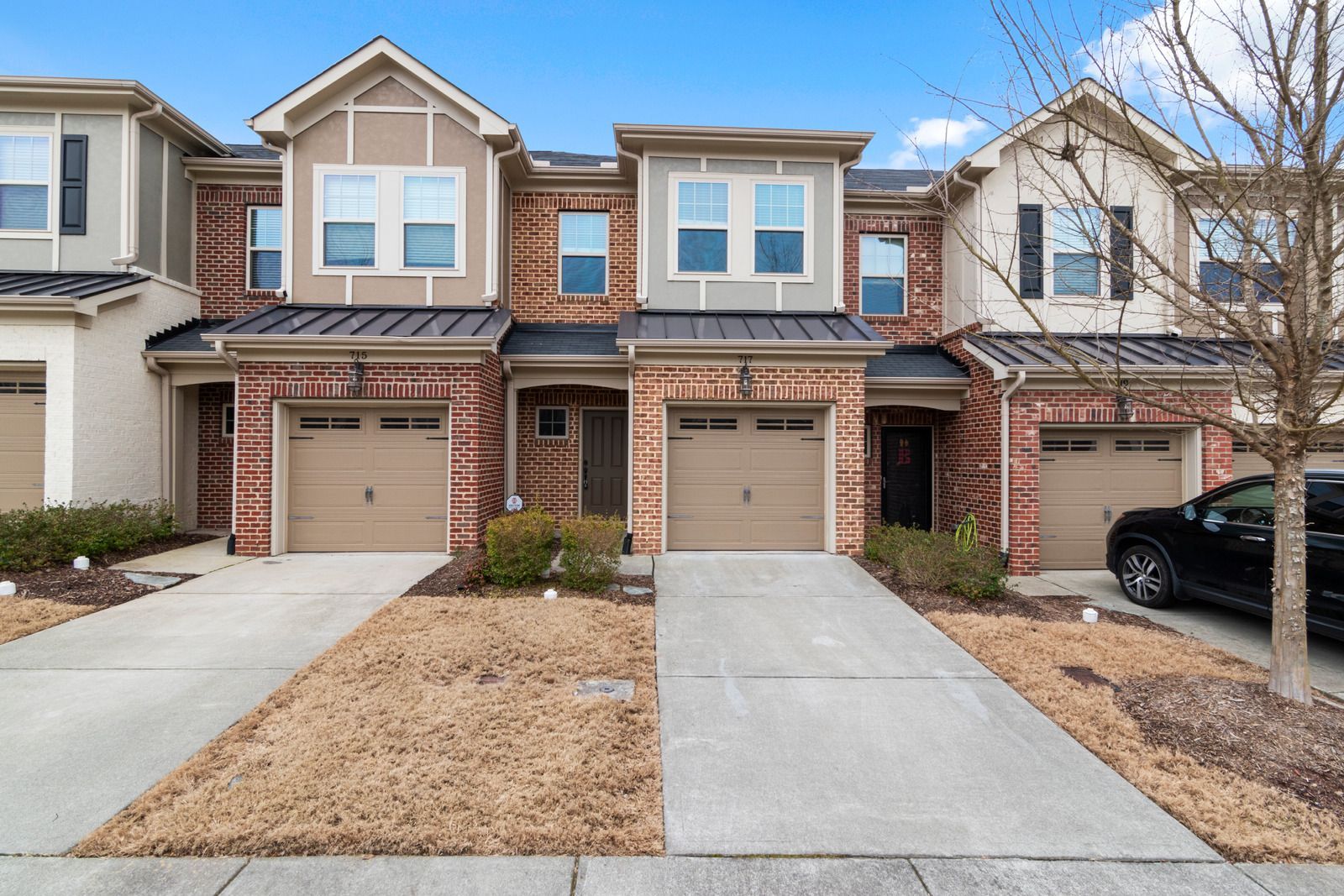 Townhomes with brick exteriors, tan garage doors, and concrete driveways under a cloudy sky.