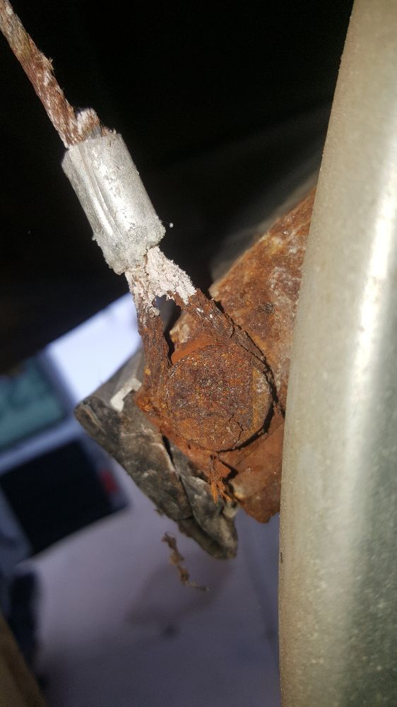 Rusty broken metal clamp on a wire next to a beige pole against a dark background