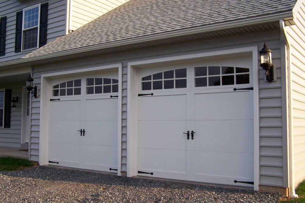 Two white garage doors with small windows on a house exterior