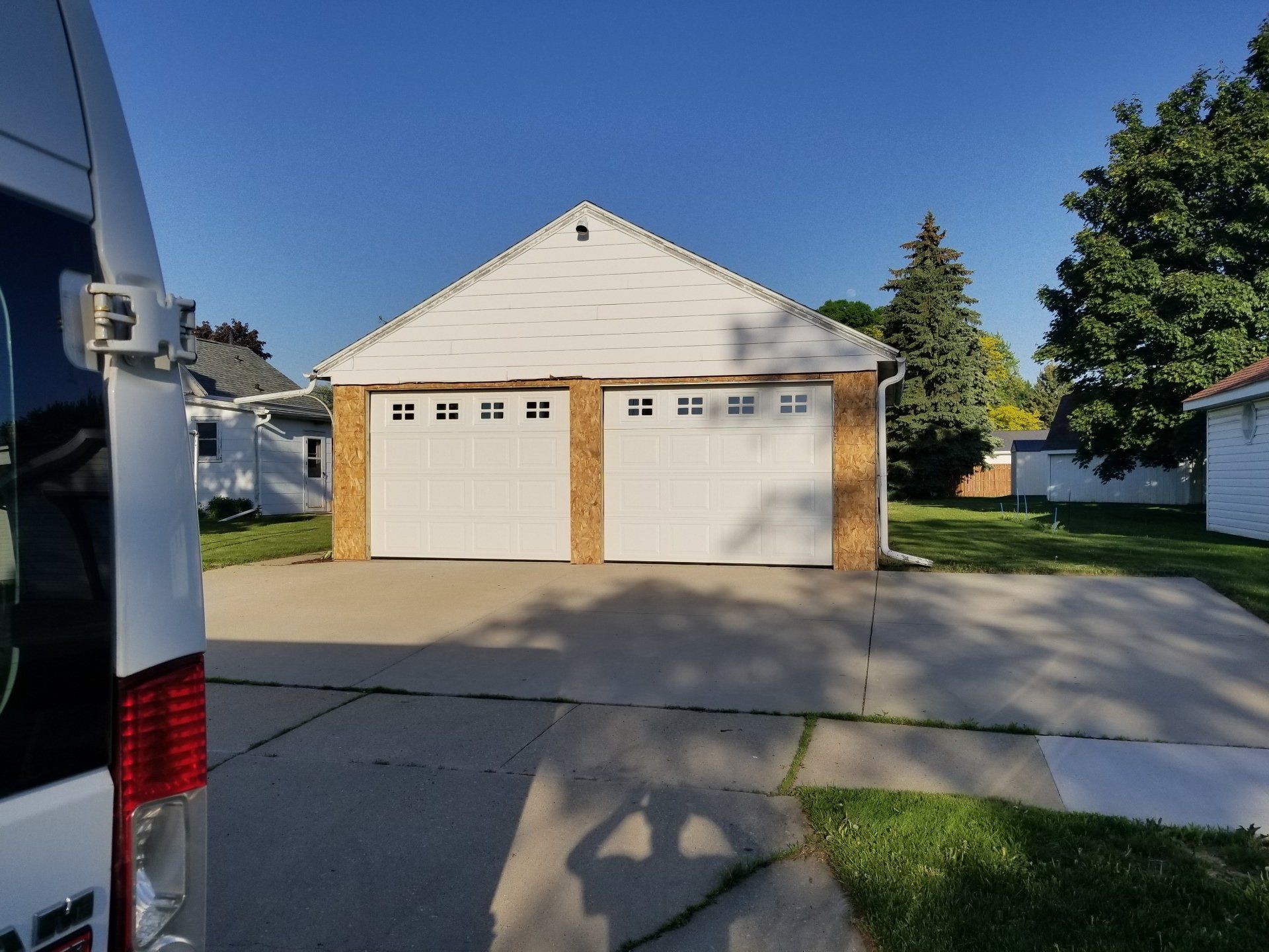 Suburban house with a two-car garage, driveway, and lawn in bright daylight.