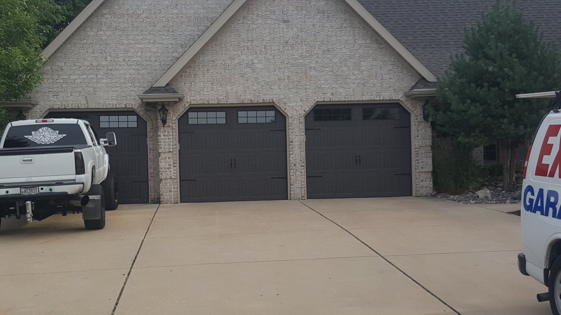 Suburban house with two dark garage doors and two work trucks parked in the driveway.