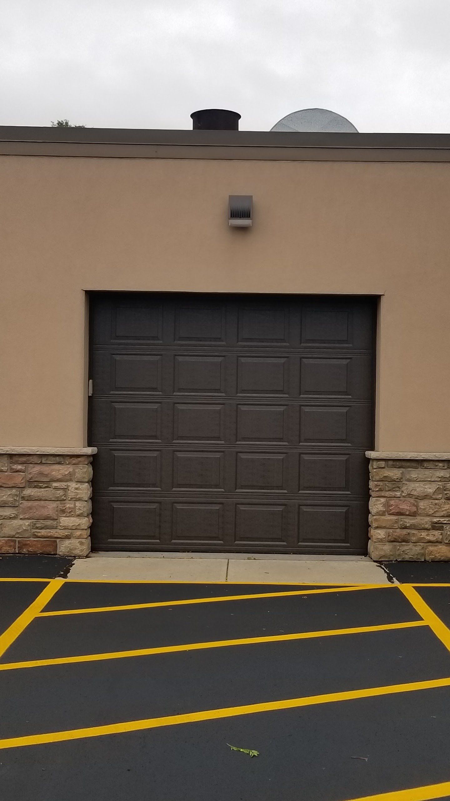 Brown garage door on a beige building with yellow striped pavement markings in front.
