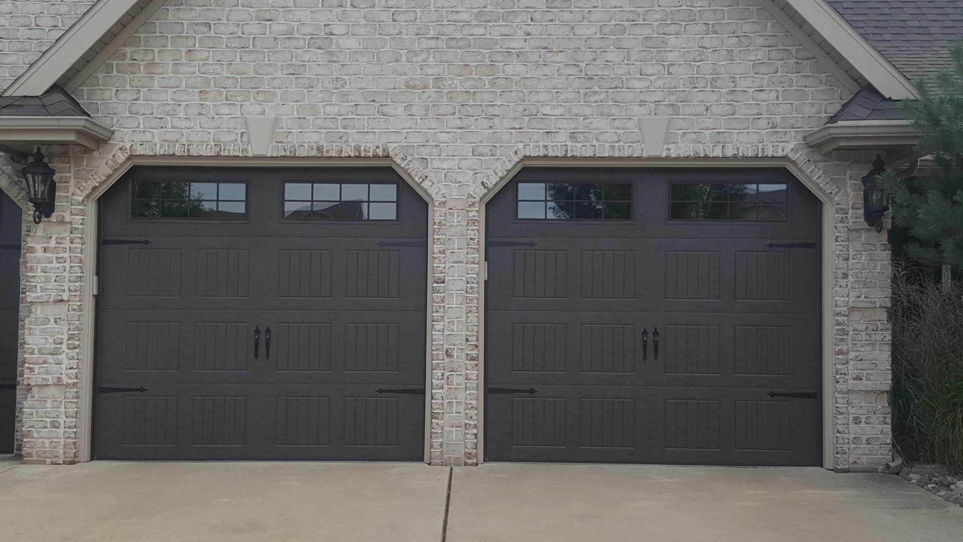 Two dark gray garage doors on a brick house with a concrete driveway in front