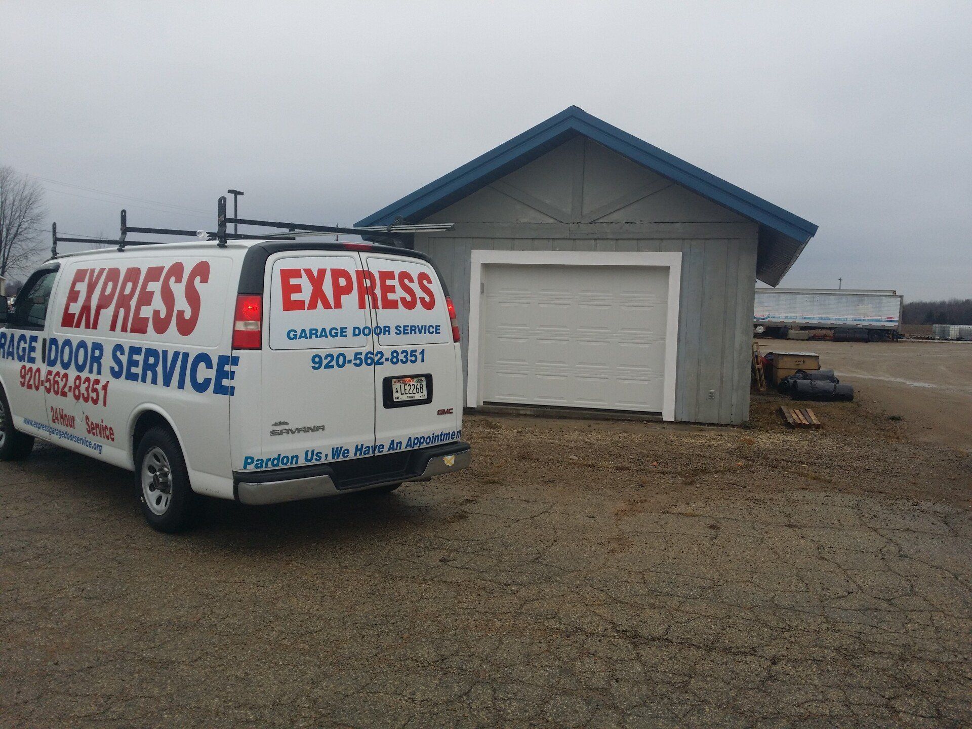 White Express plumbing service van parked beside a small blue-gray garage on a gravel lot.