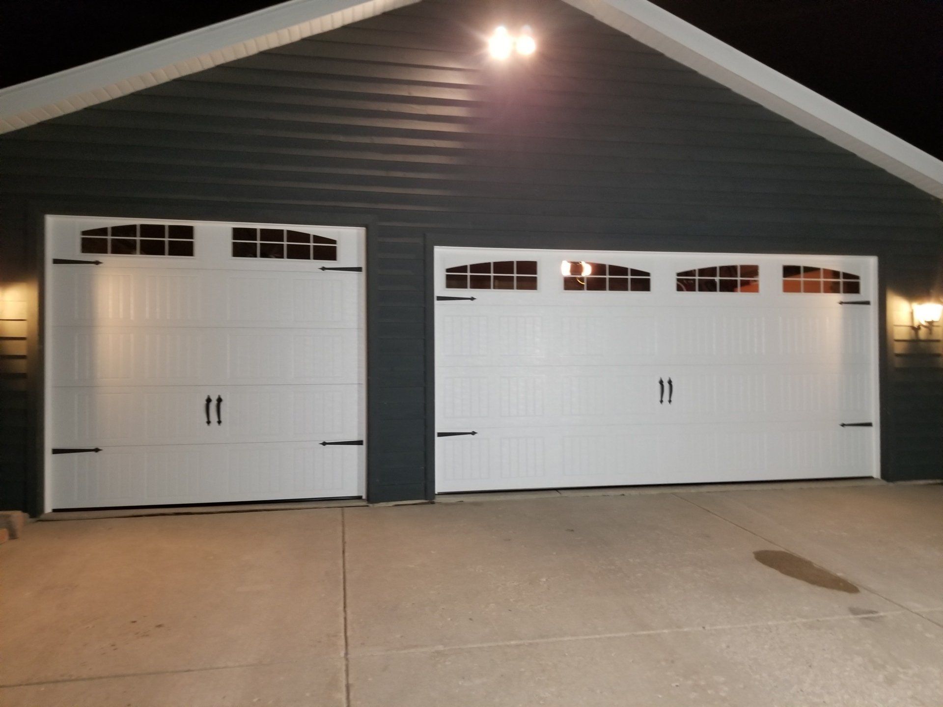 Two white garage doors on a dark house at night, lit by an exterior porch light.