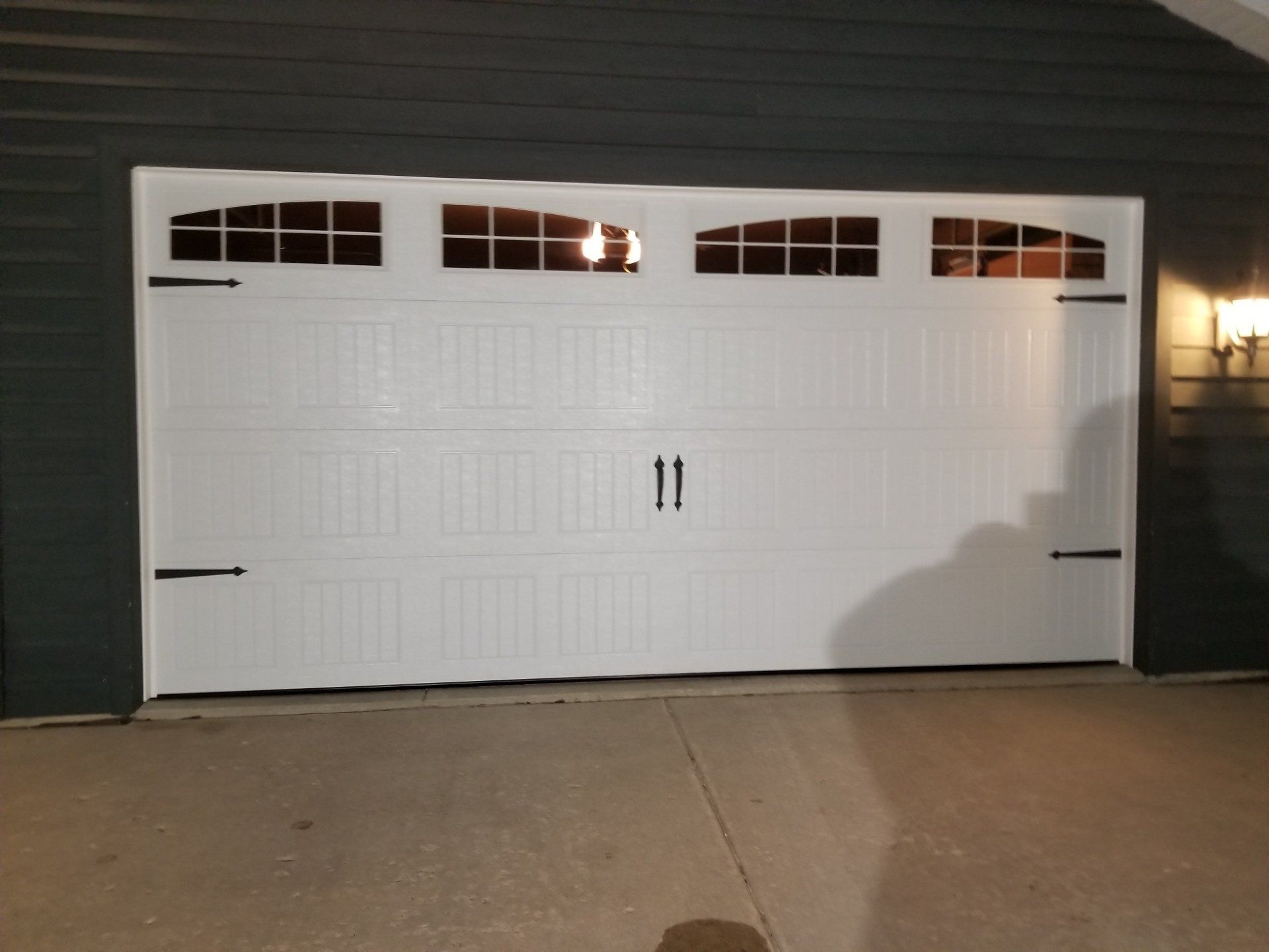 White double garage door with arched windows at night, viewed from a driveway