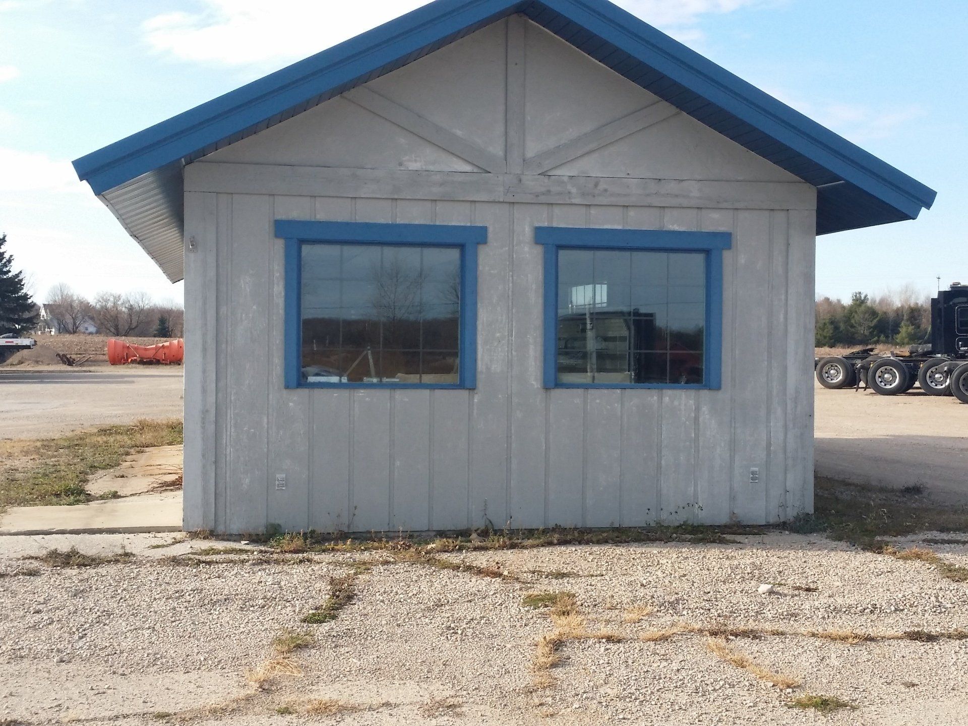 Small gray building with blue trim and windows on a gravel lot