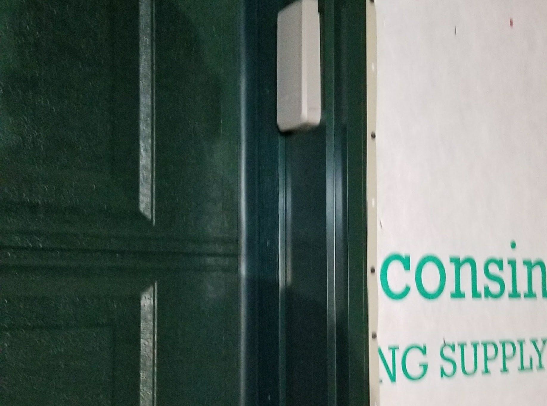 Green door beside a white wall with teal signage reading “consi…” and “NG SUPPLY”