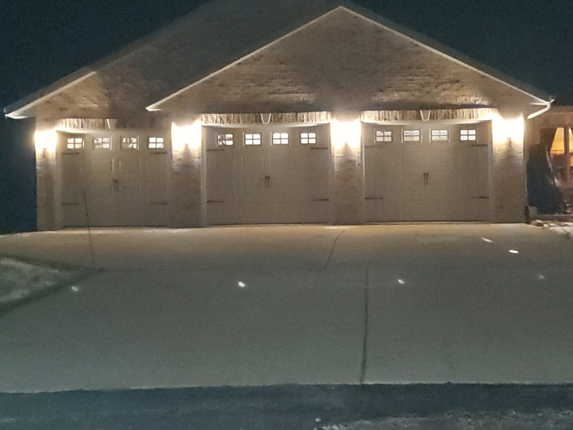 Snow-covered suburban house with three garage doors lit warmly at night