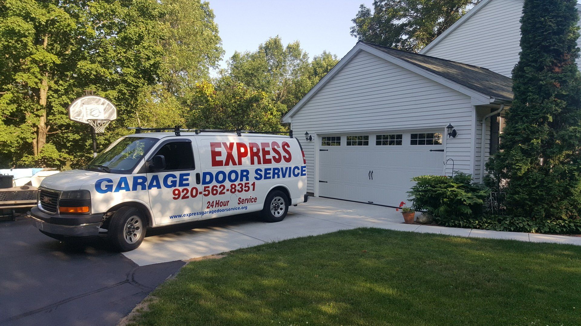 White service van with “Garage Door Service” parked in a driveway beside a house and garage.