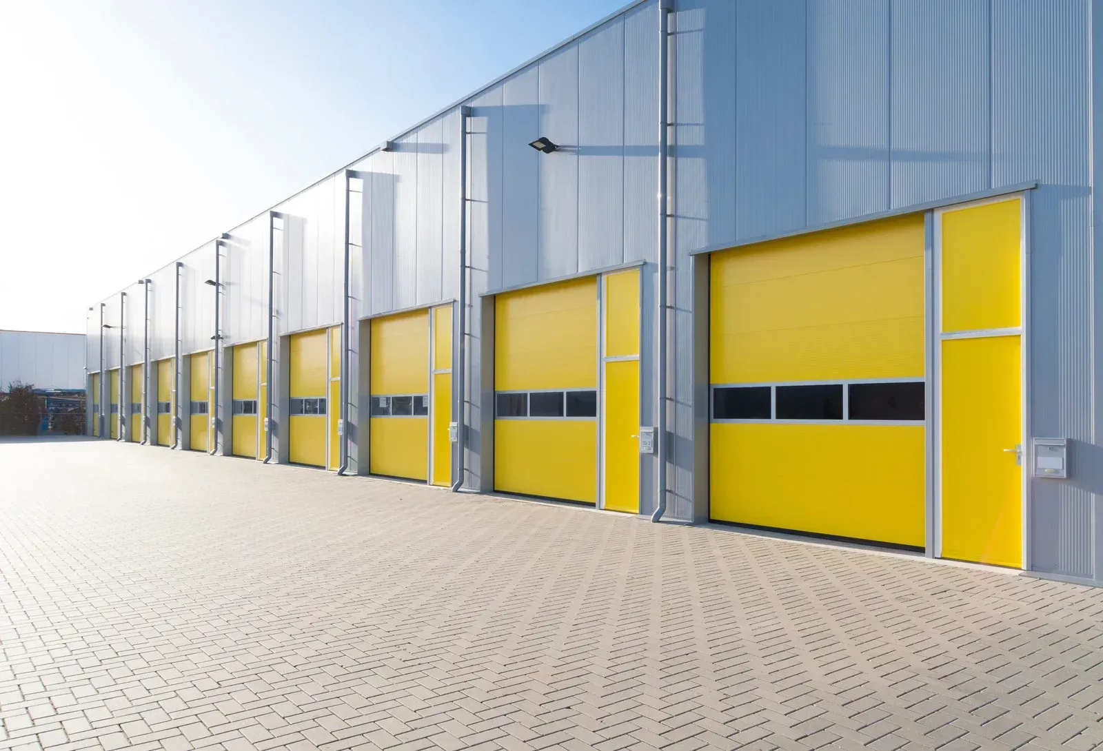 Exterior of a warehouse with a row of yellow loading dock doors, set against a blue sky.