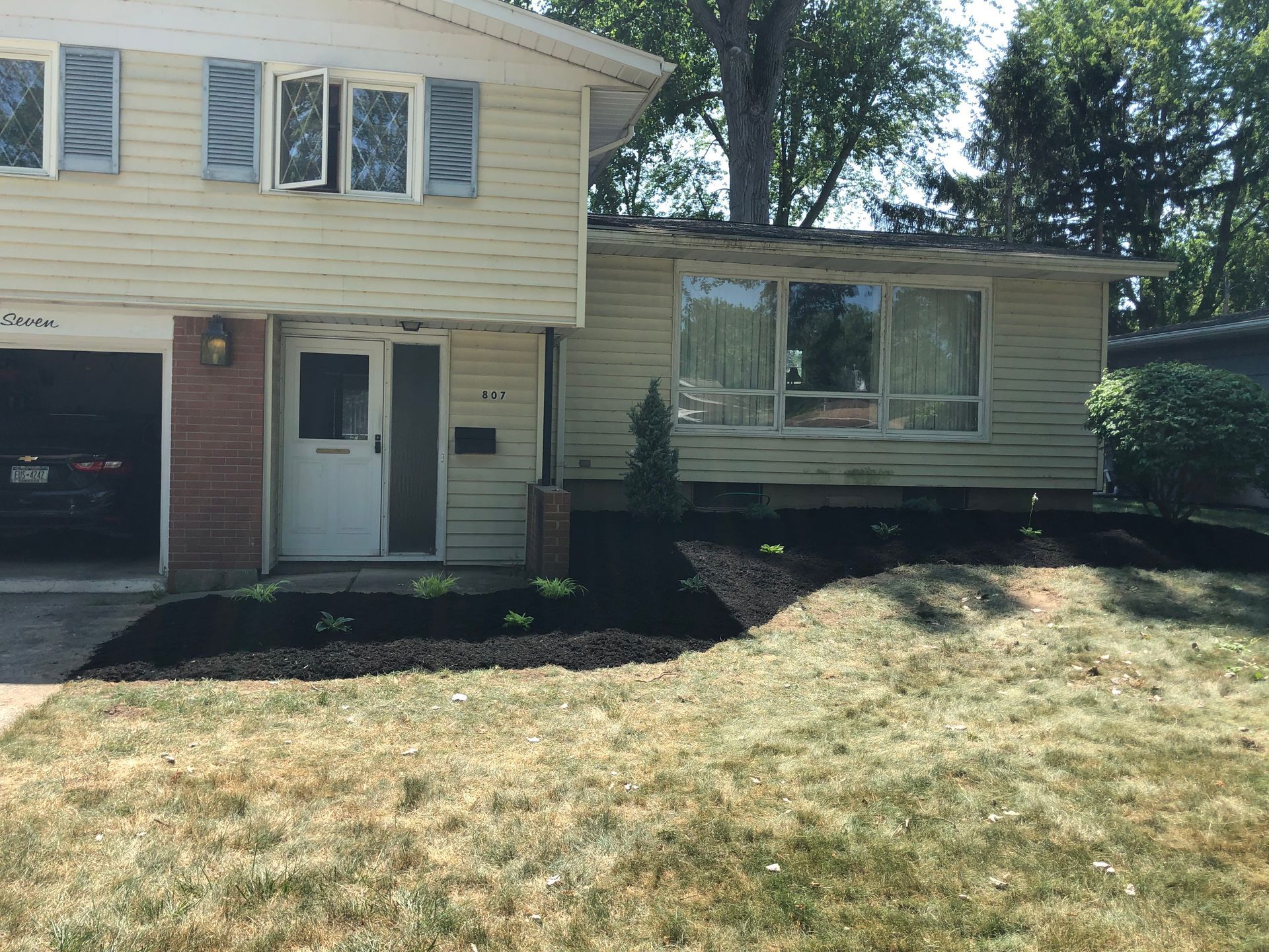 A two-story house with cream-colored siding, a garage, a front door, and a garden bed with fresh mulch in the front yard.