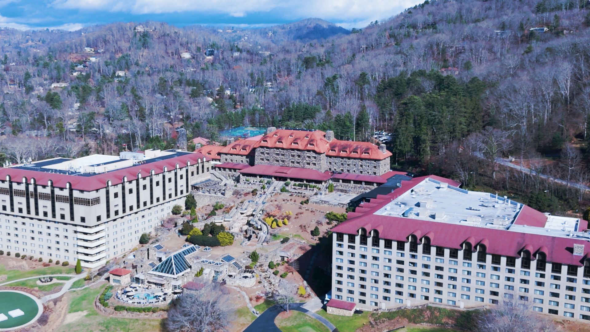 Aerial view of a large mountain resort complex with red roofs, white buildings, and wooded hillsides.