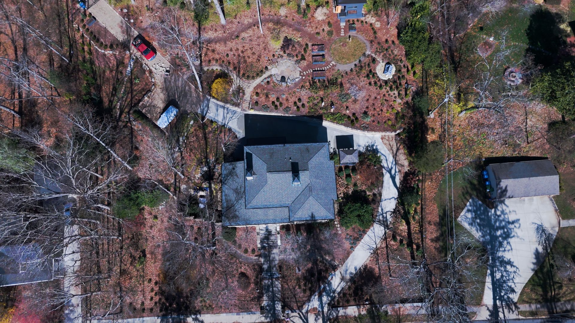 Aerial view of a house with a dark roof and a driveway beside trees and a parked car.