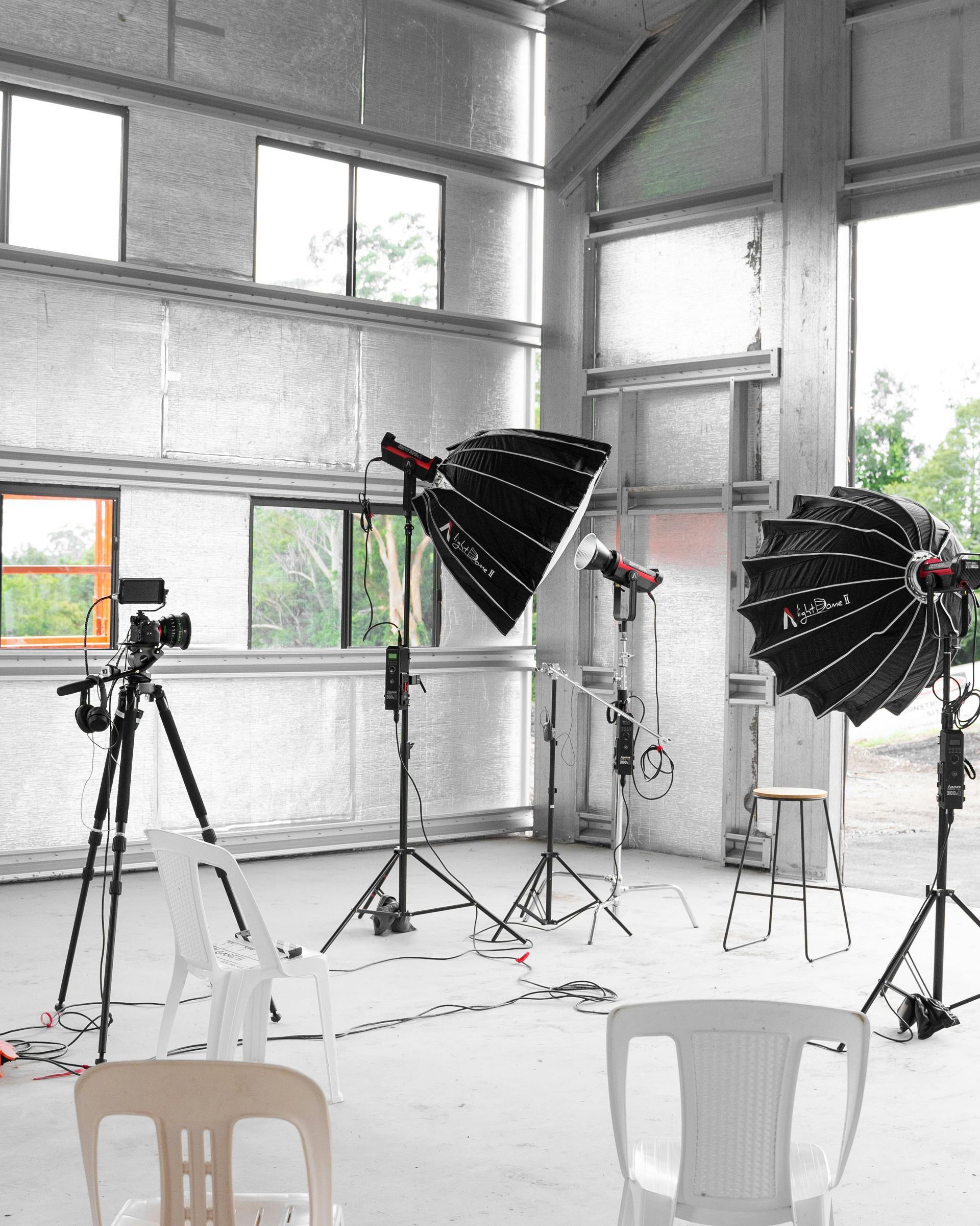 Photography studio with cameras on tripods, softbox lights, and white chairs in a bright room