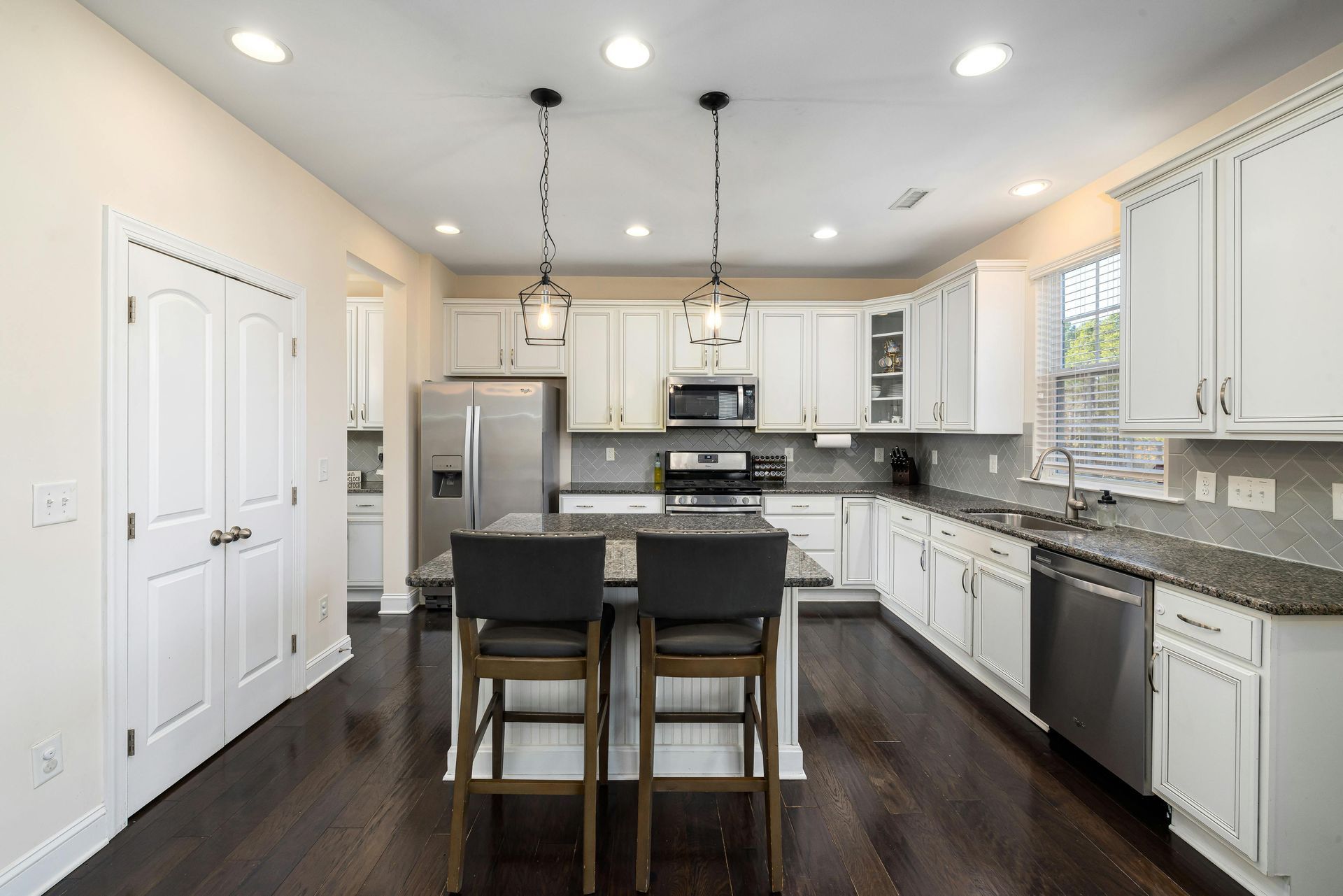 Modern white kitchen with dark island, stainless appliances, pendant lights, and dark wood floors