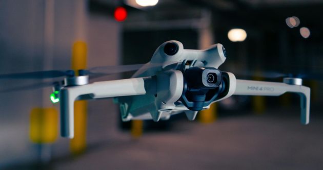 White drone flying indoors in a dim garage, with blurred lights in the background