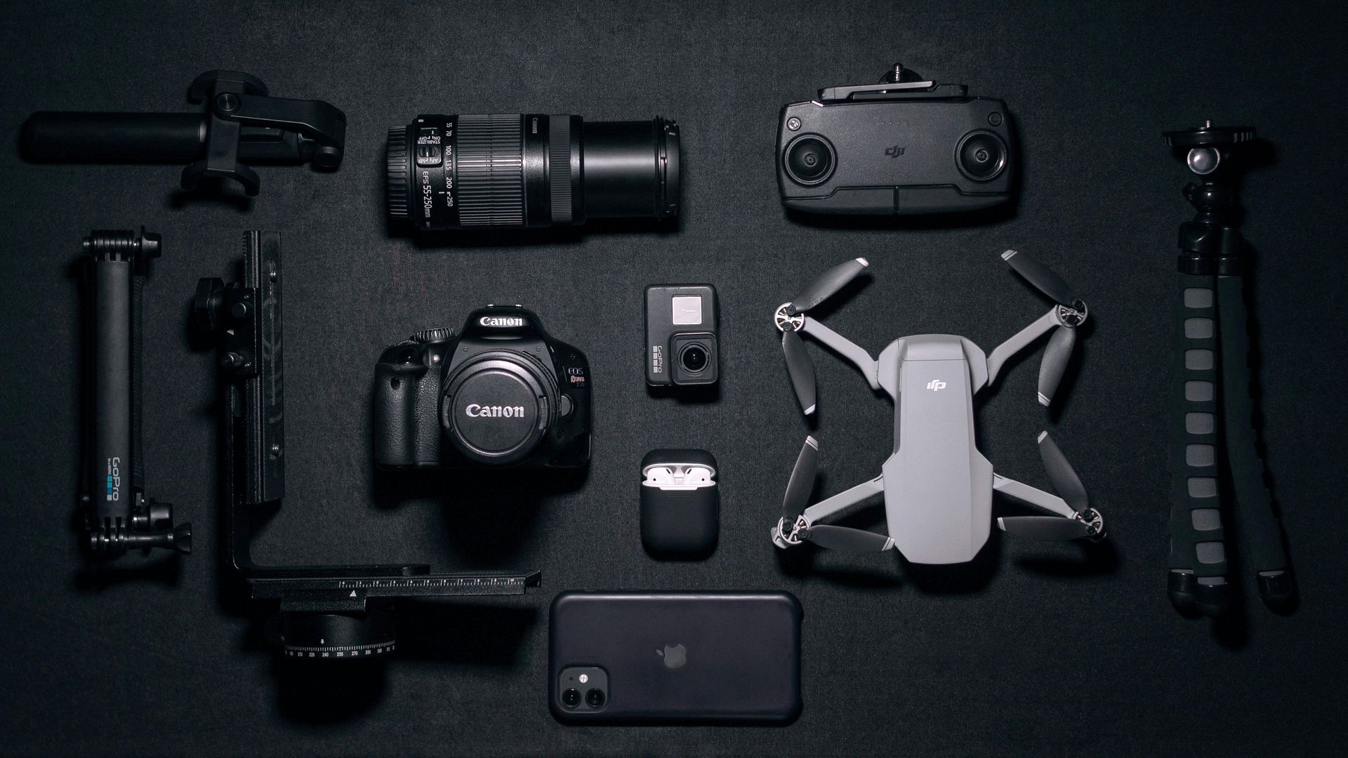 Camera gear and drone neatly arranged on a dark surface, including lens, camera body, controller, and accessories