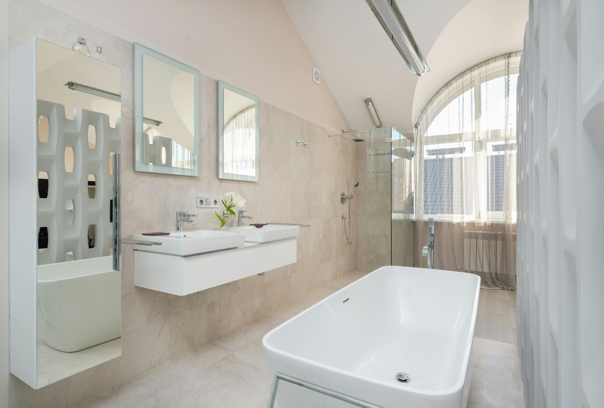 Bright modern bathroom with a freestanding tub, floating vanity, mirrors, and arched window.