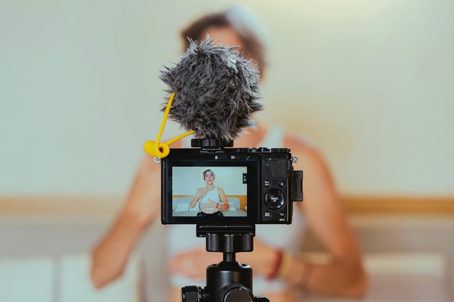 Camera on tripod filming a person speaking indoors with a large microphone in the foreground