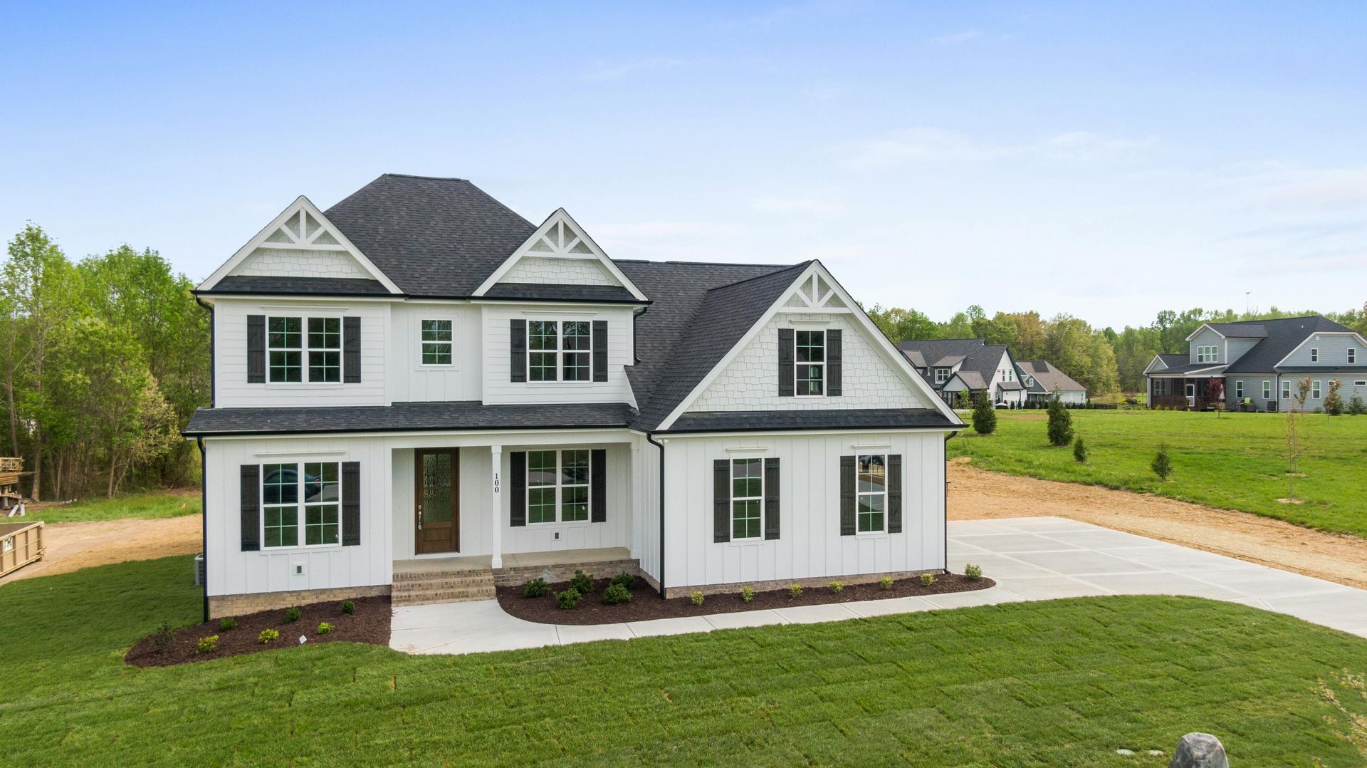 White two-story house with gray roof and green shutters on a grassy lot with a driveway