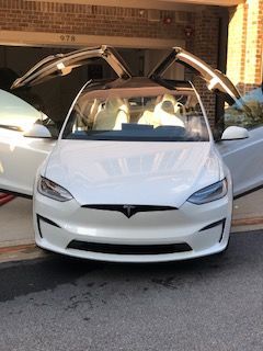 White Tesla with both falcon-wing doors open, parked outside a brick building.