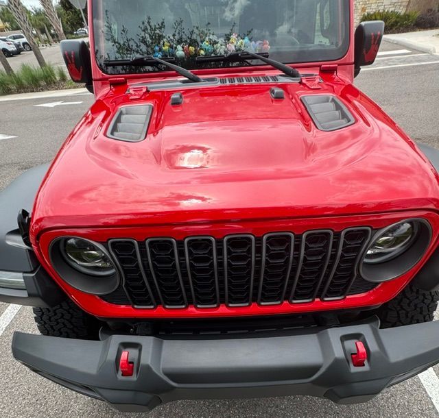 Red Jeep SUV front view with bright red hood, black grille, and parked outdoors on pavement