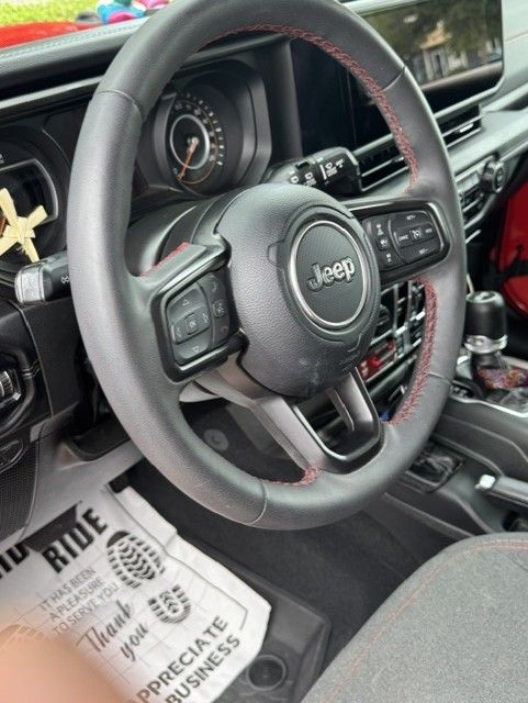 Jeep steering wheel and dashboard interior with black accents and red trim, seen from the driver’s seat