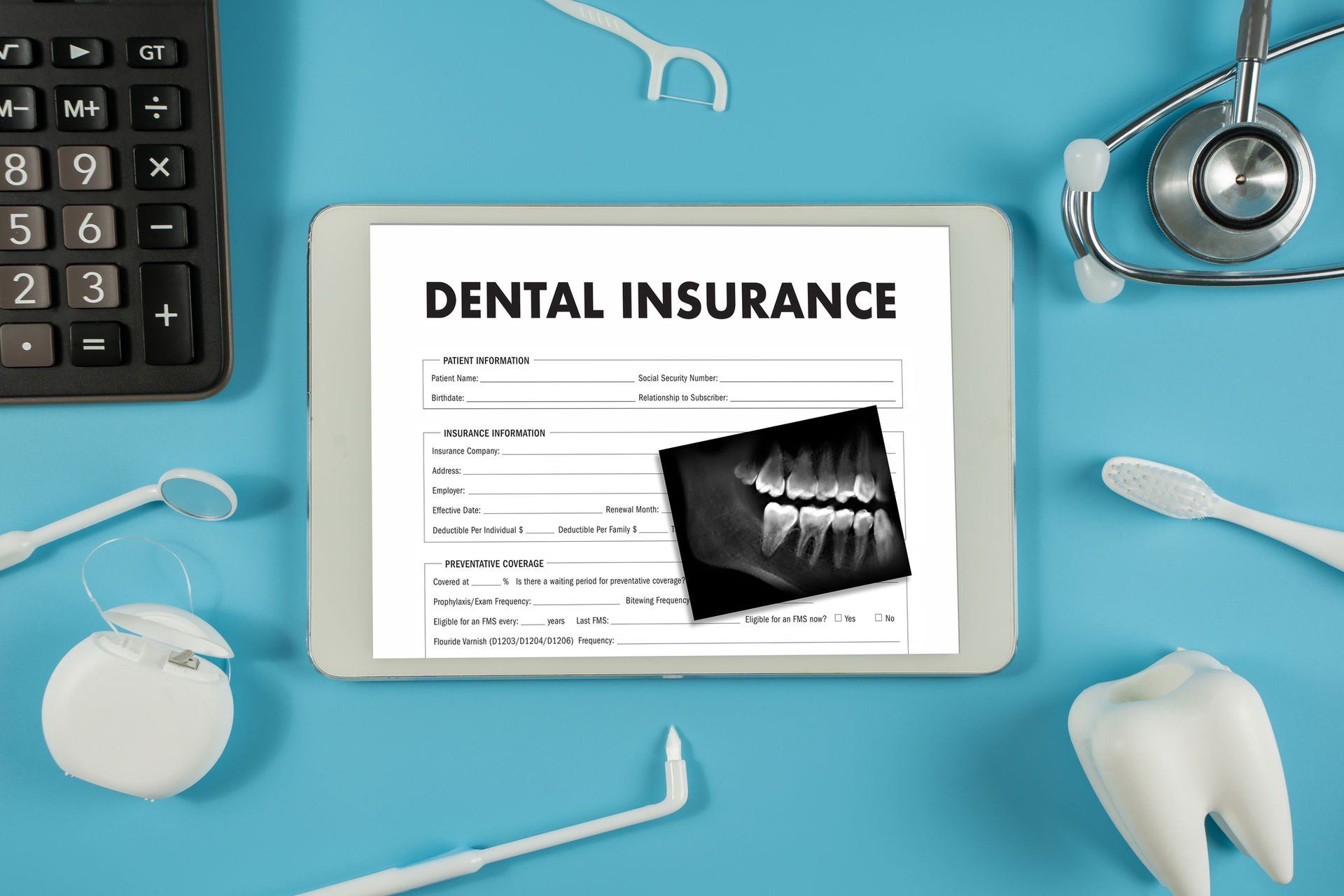 Dental insurance form on tablet with dental tools, calculator, and x-ray on blue surface.