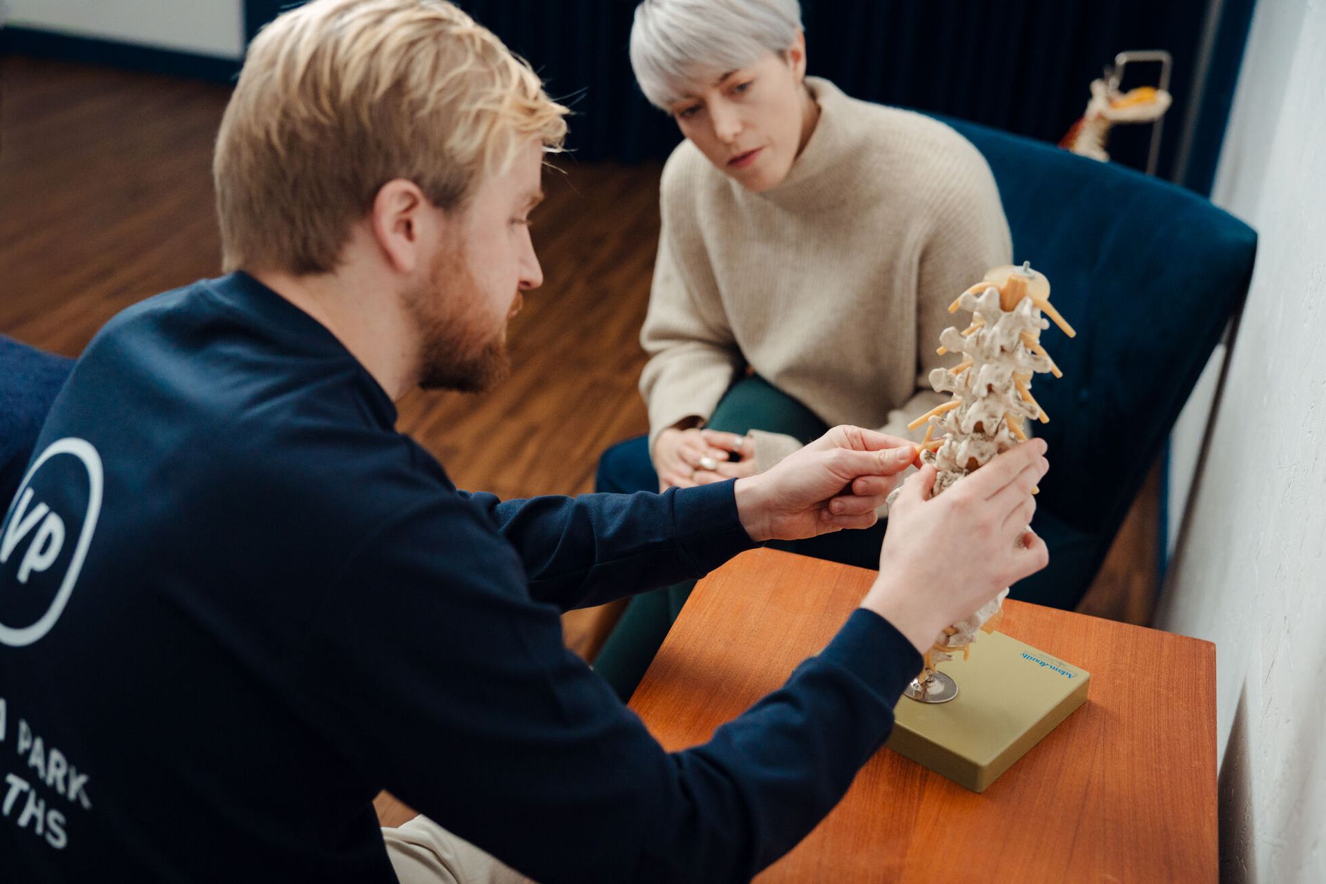Male osteopath shows a female patient model of the human spine to demonstrate the treatment.