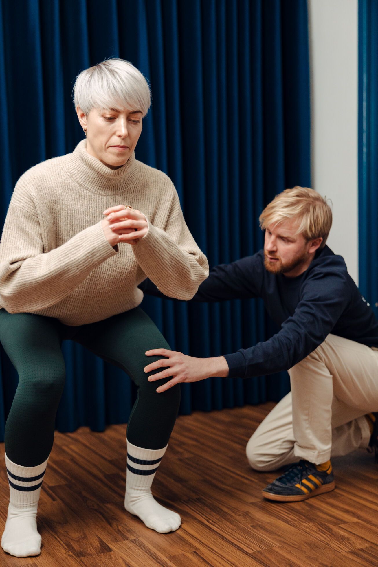 Patient with short silver head in a quat position while the osteopath crouches down assessing her position and suggesting adjustments.