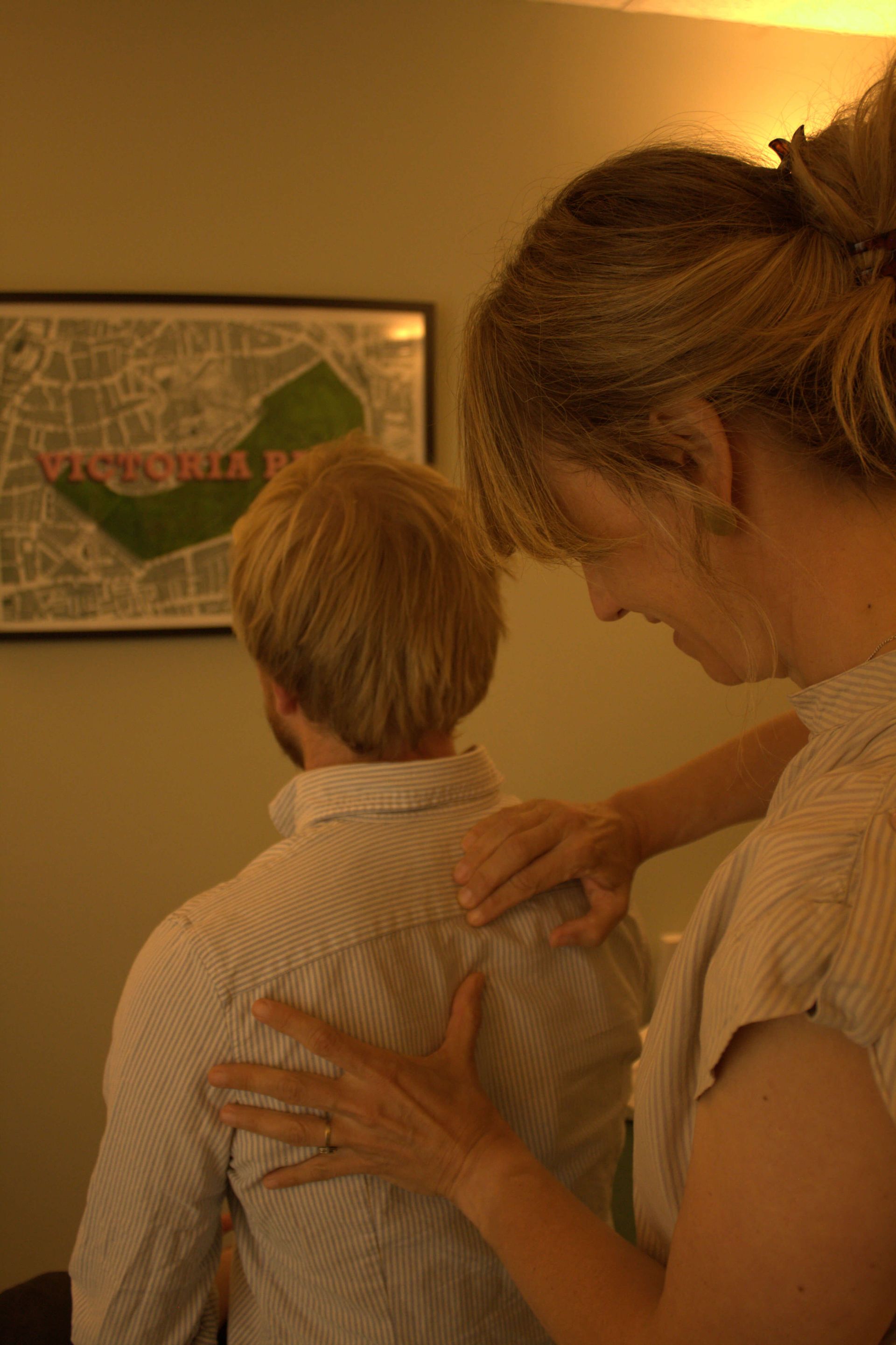 Osteopath treats patient, massaging back.