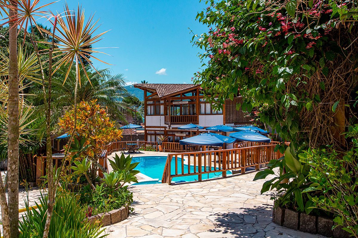 Deck de madeira com duas espreguiçadeiras, palmeiras tropicais e vista para o mar sob um céu azul.