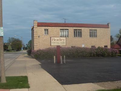 Brick building with a roadside sign and parking lot under a cloudy sky