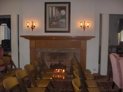 Living room with fireplace, rows of chairs, wall sconces, and a framed painting above the mantel