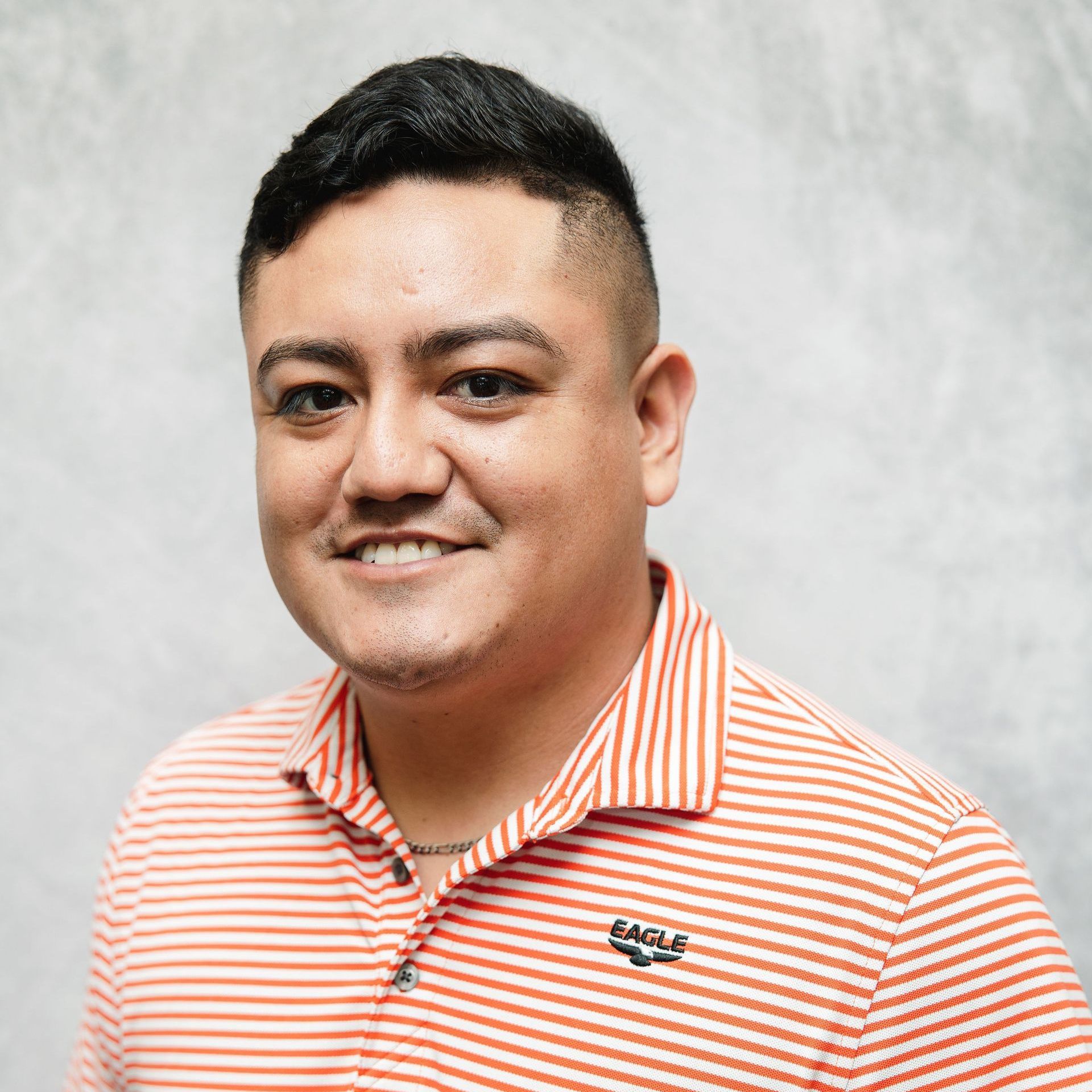 A man in an orange and white striped shirt is smiling for the camera.