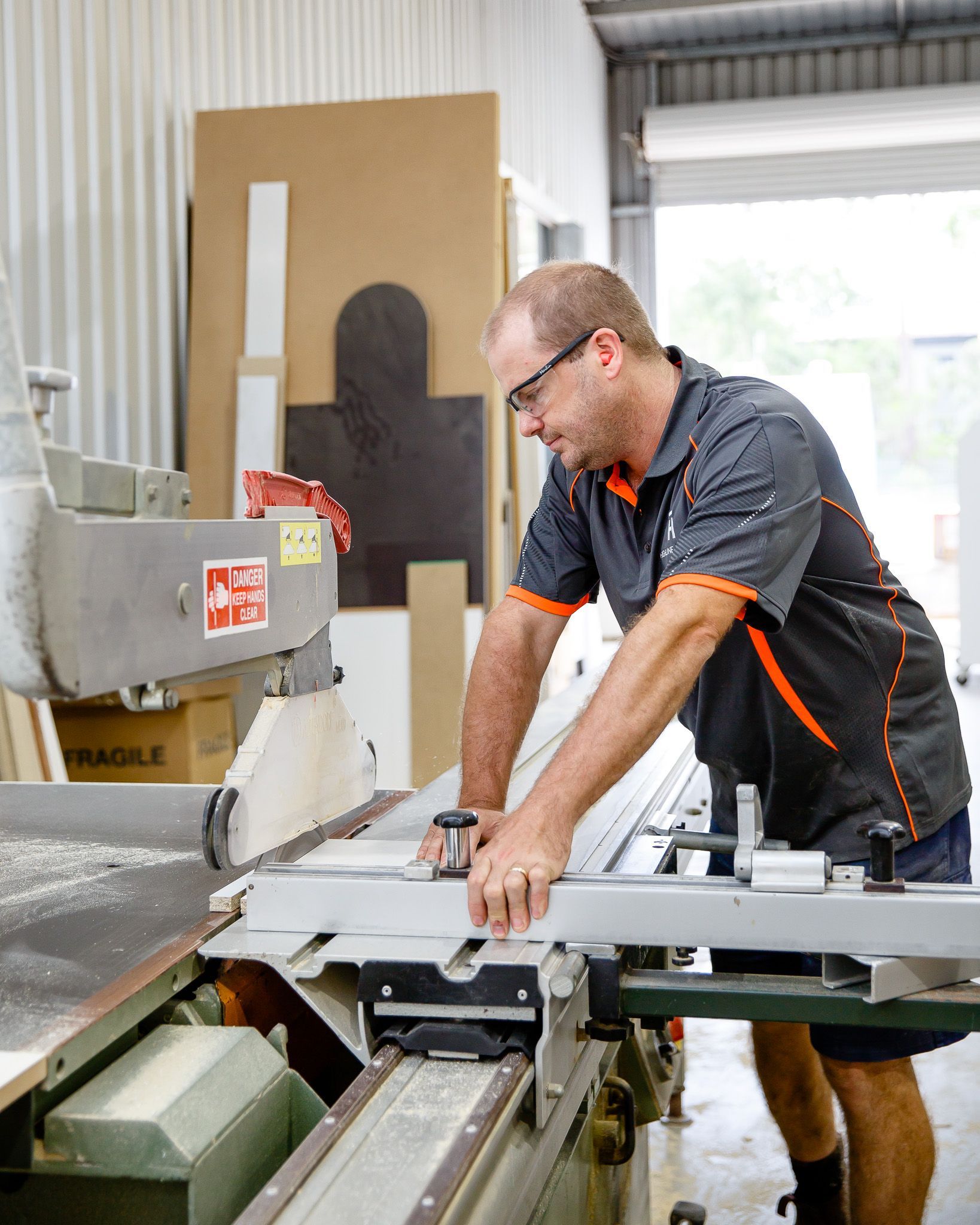Man in Shop Using a Saw; Wearing Glasses and Work Shirt — Kitchens Factory Direct in Port Macquarie, NSW