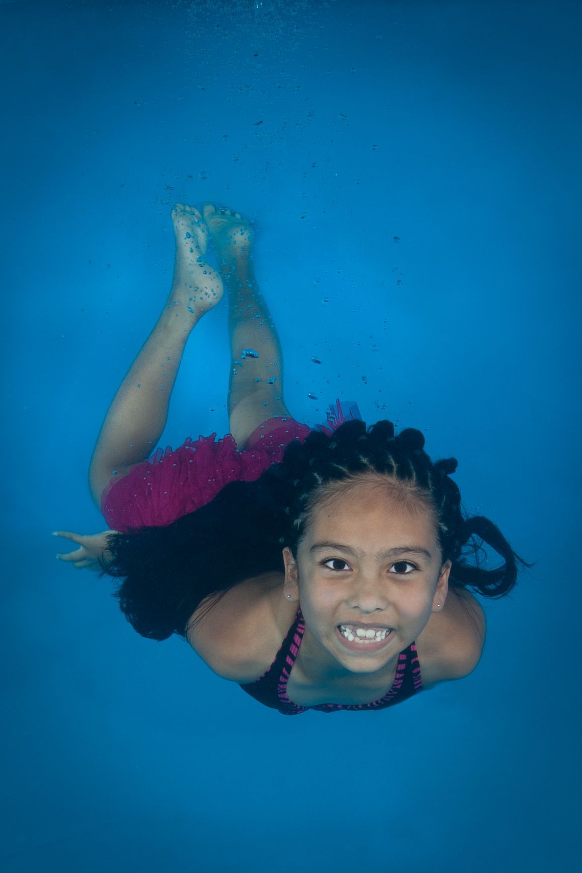 a little girl is swimming underwater in a pool in swim lessons .