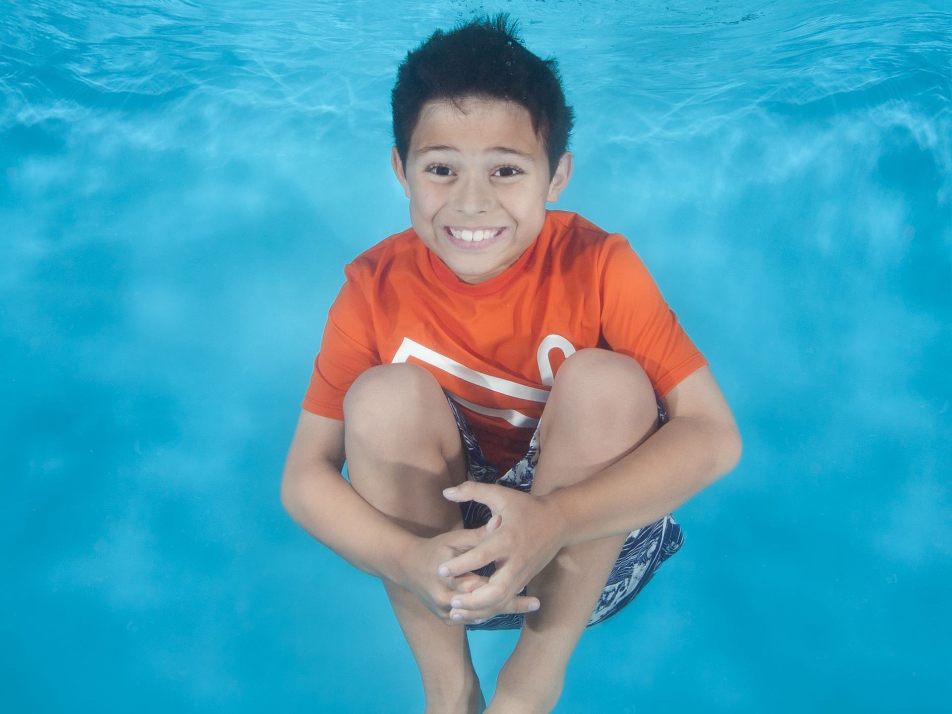 a young boy is kneeling underwater in a swimming pool for swim lessons