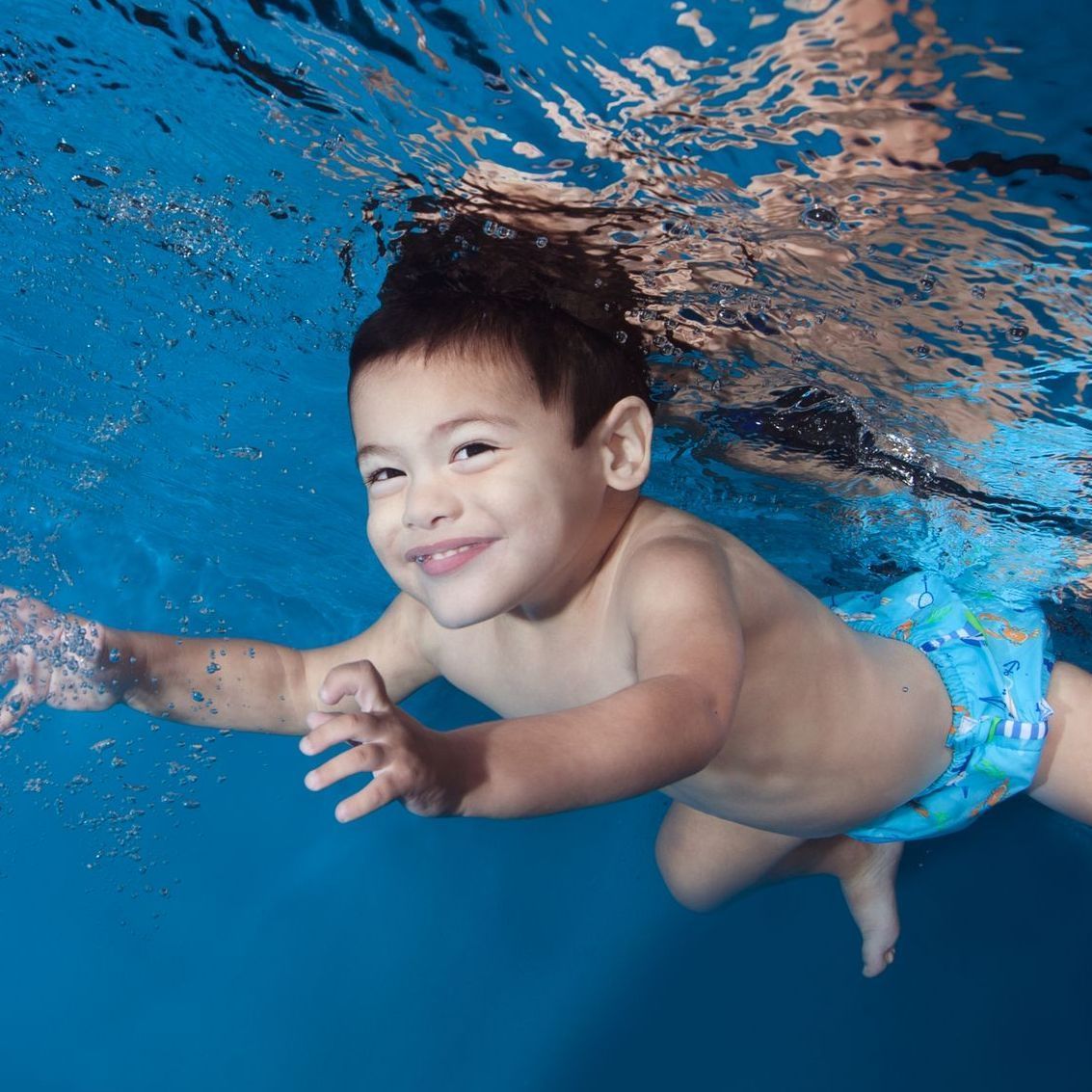 a young boy is smiling while swimming underwater in a pool during swim lessons