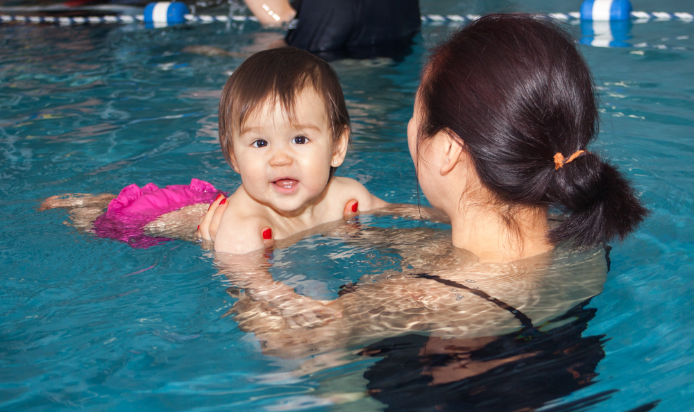 a woman is holding a baby in a swimming pool for swim lessons