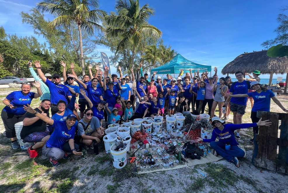 a large group of people are posing for a picture on a beach doing a clean up for a swim school