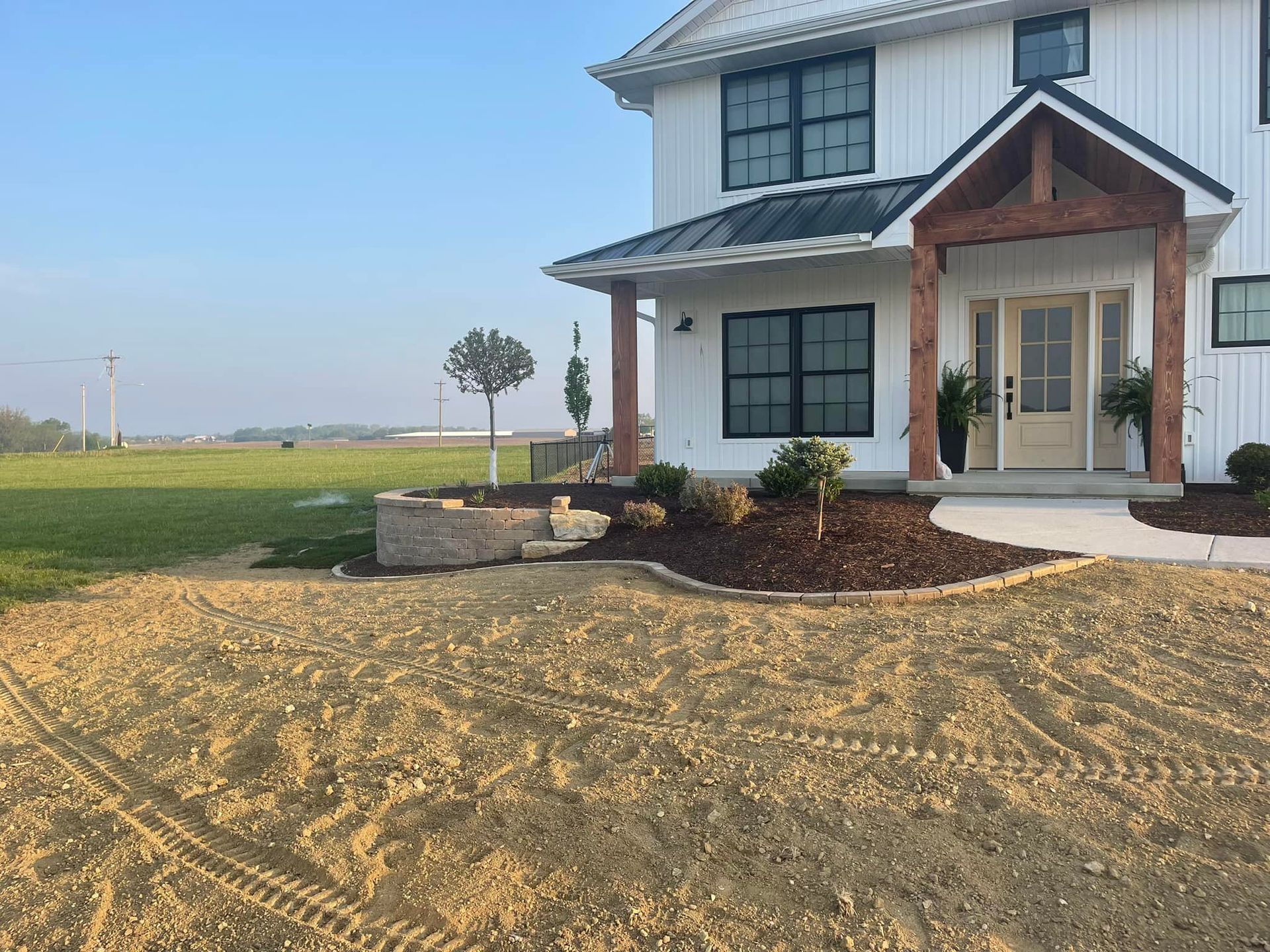 White farmhouse with black windows, a covered porch, and a yard under construction.