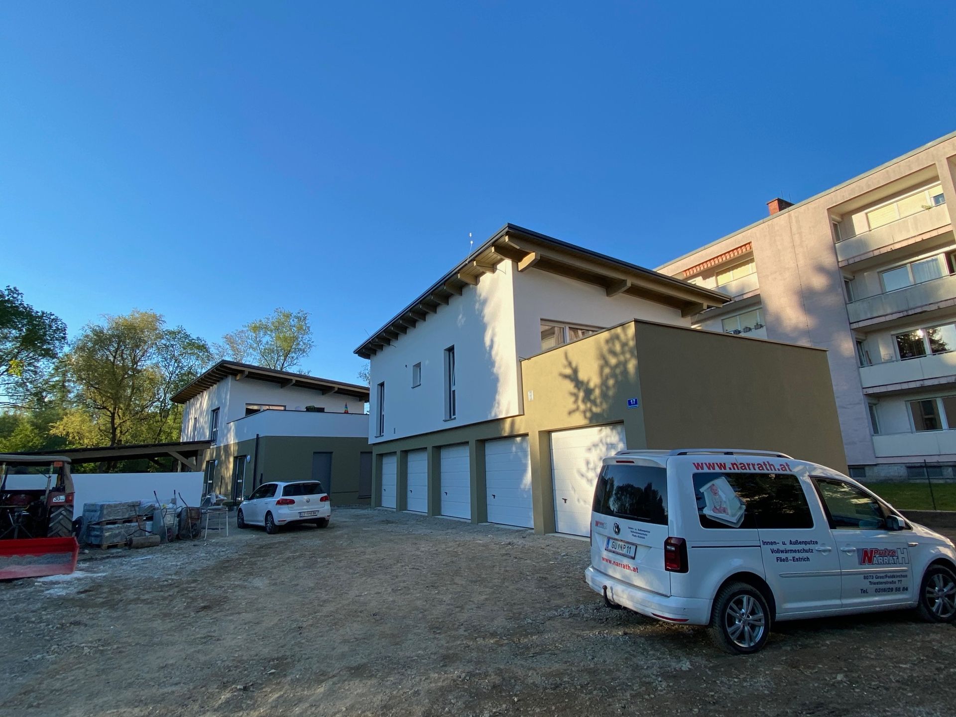 Neue Wohnhäuser mit Garagentoren unter strahlend blauem Himmel, ein weißer Lieferwagen und ein Pkw parken