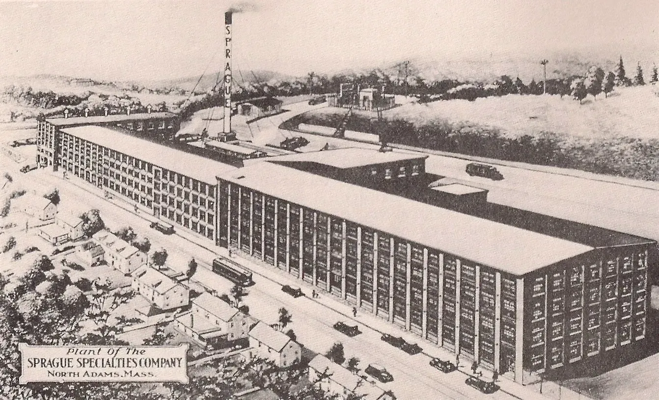 Black-and-white aerial rendering of a long multi-story industrial building with surrounding roads and trees