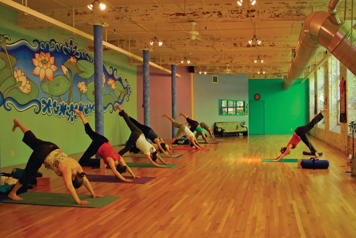 People doing yoga stretches in a bright studio with wood floors and colorful wall murals