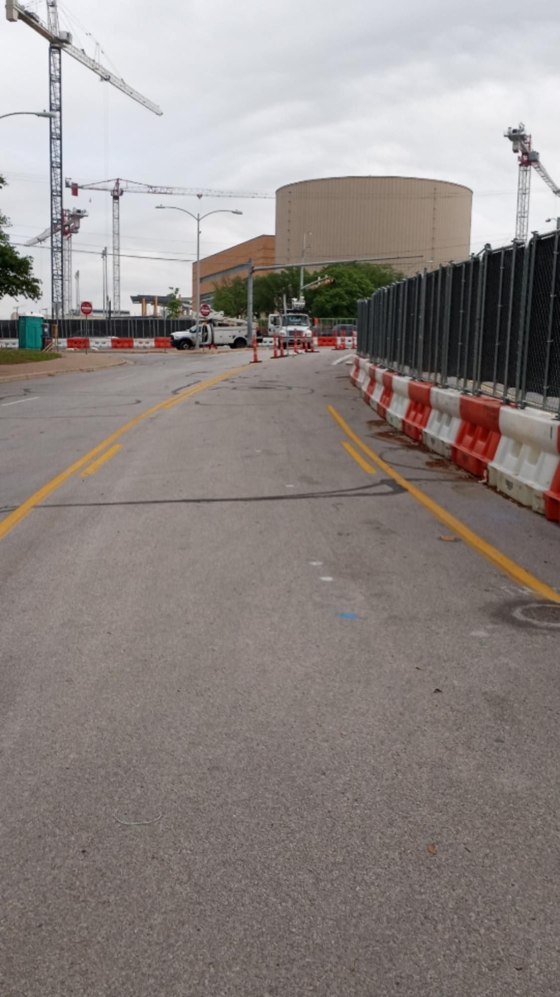 A road with a fence and a large building in the background ,traffic control cones