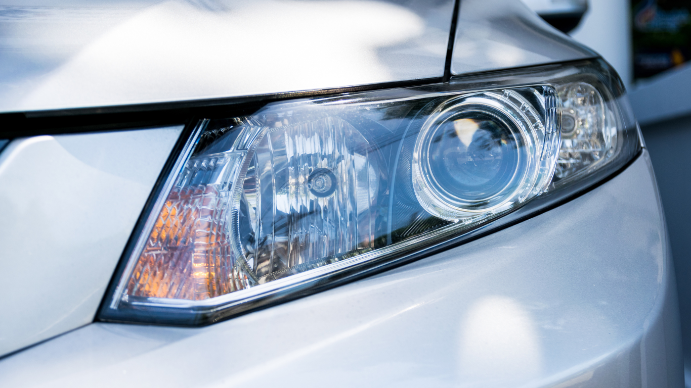 Close-up of a silver car’s front headlight and hood with chrome detailing.